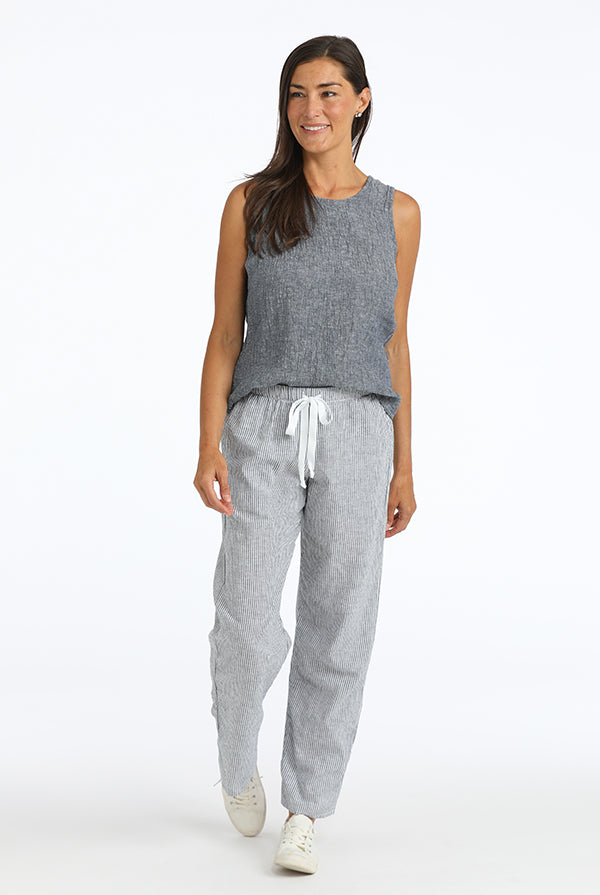 Woman wearing a gray sleeveless top and striped linen  pants on a white background