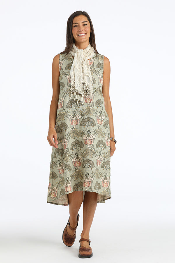 Woman wearing a sleeveless green floral dress with a scarf on a white background