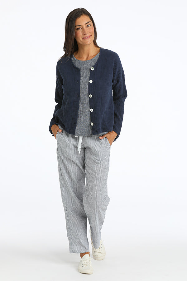 Woman wearing a navy cardigan over a gray shirt with gray pants on a white background