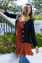 Woman wearing a black cardigan over a rust-colored dress with a white background