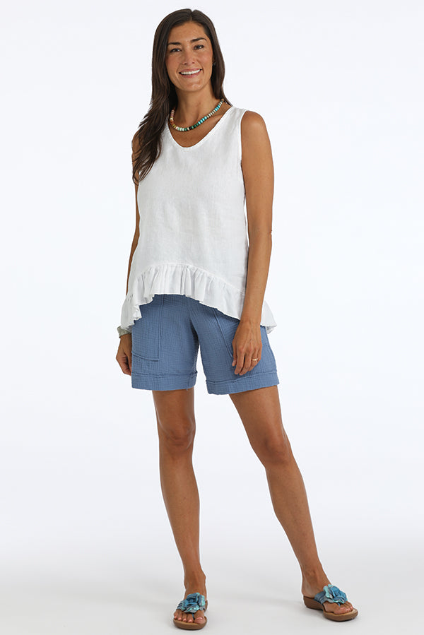 Woman wearing a white sleeveless top with ruffled hem and blue shorts on a white background